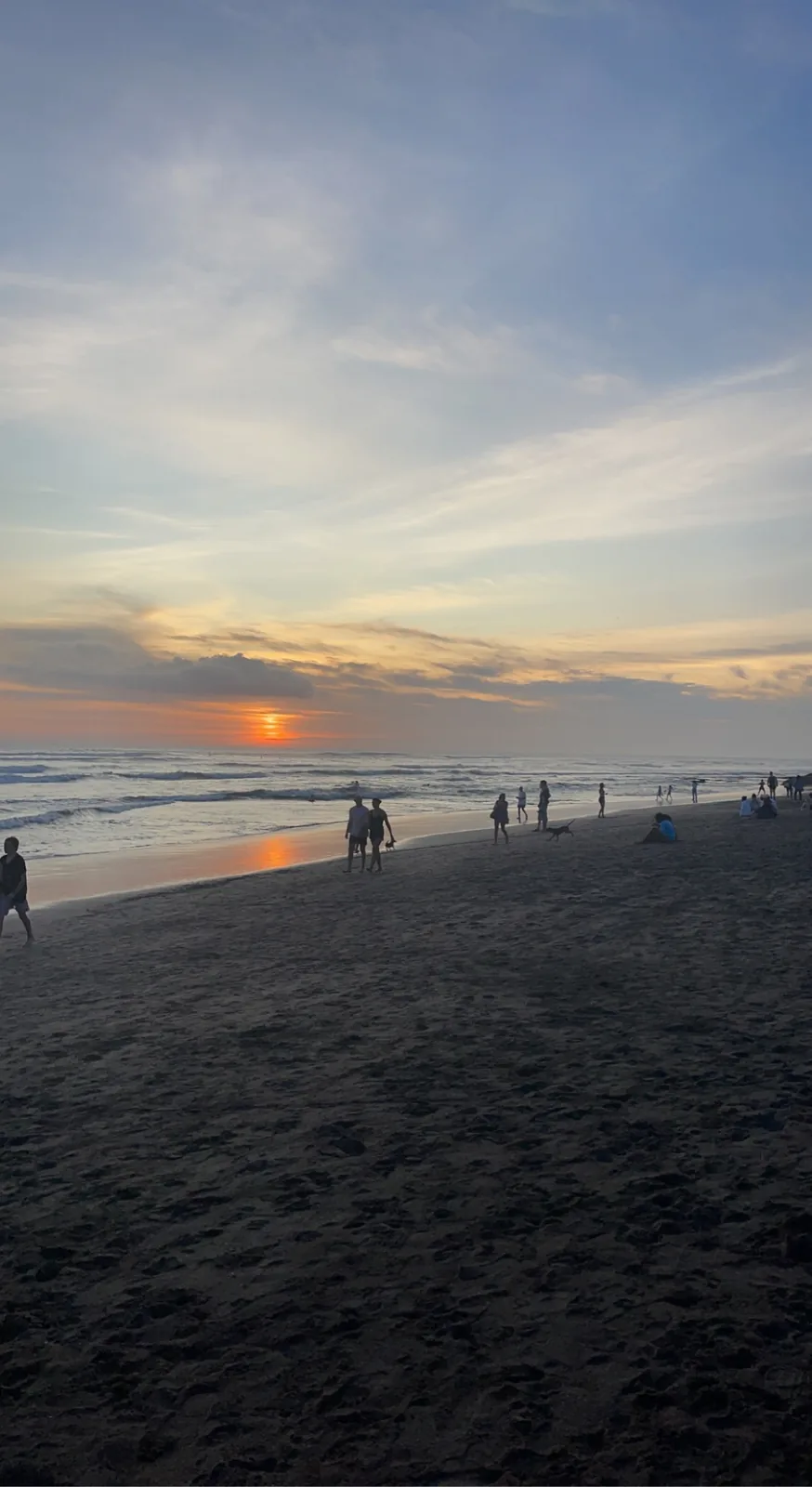 People walking on the dark sand of Canggu beach at sunset