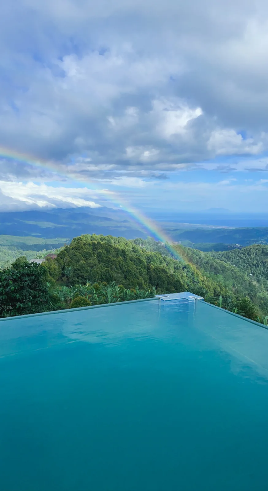 Infinity pool over the hills with a rainbow in the sky