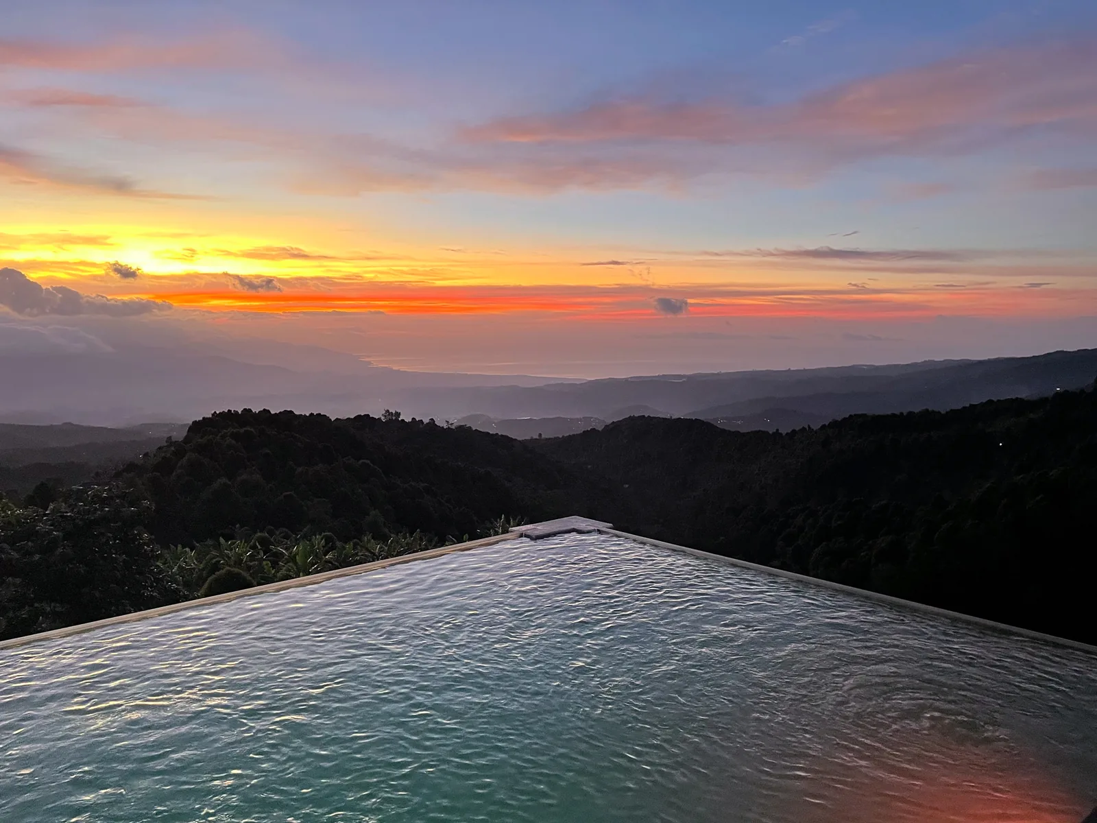 The edge of the infinity pool in Munduk at sunrise, orange sky over layered mountains
