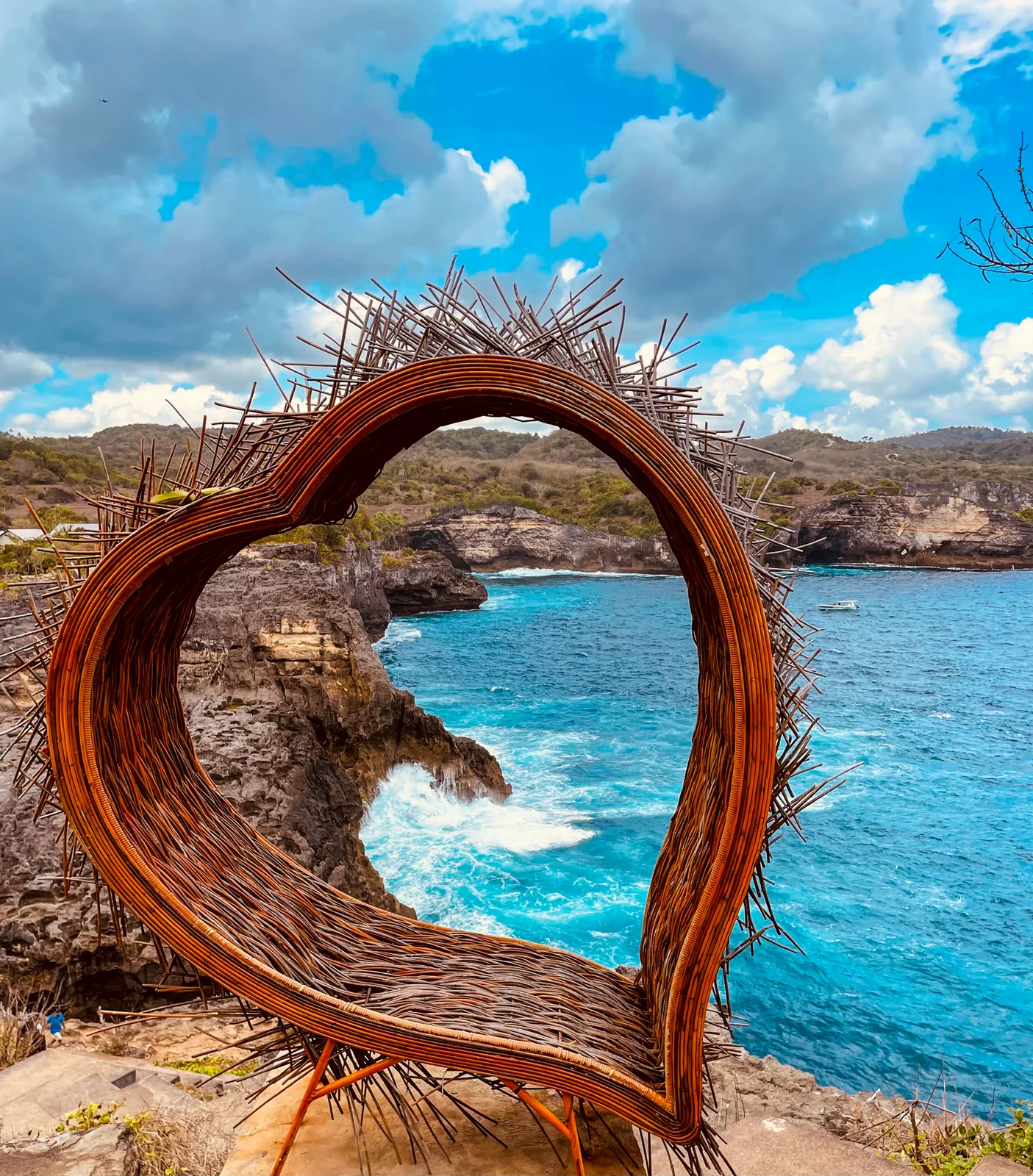 A woven wooden heart on the clifftop framing Broken Beach and its sea arch