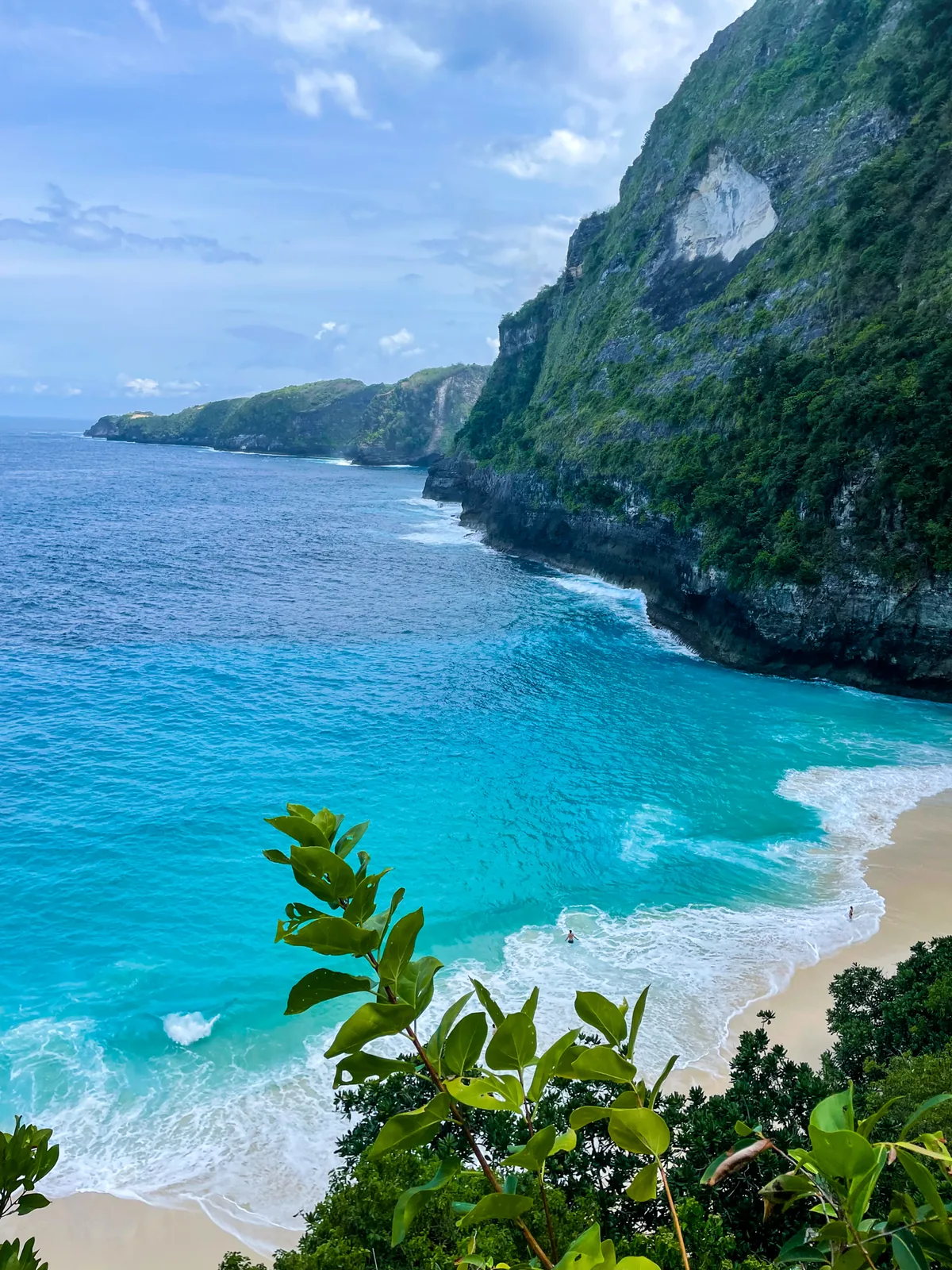 A turquoise bay and surf below tall green cliffs on Nusa Penida