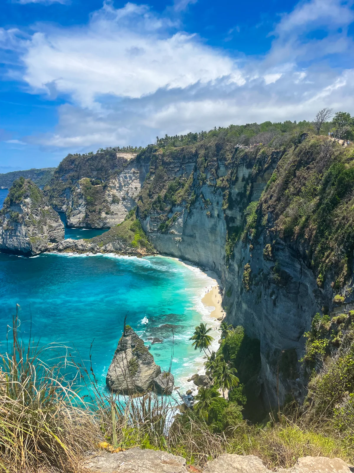 A cove with a white beach and a rock islet below tall cliffs on Nusa Penida's east coast