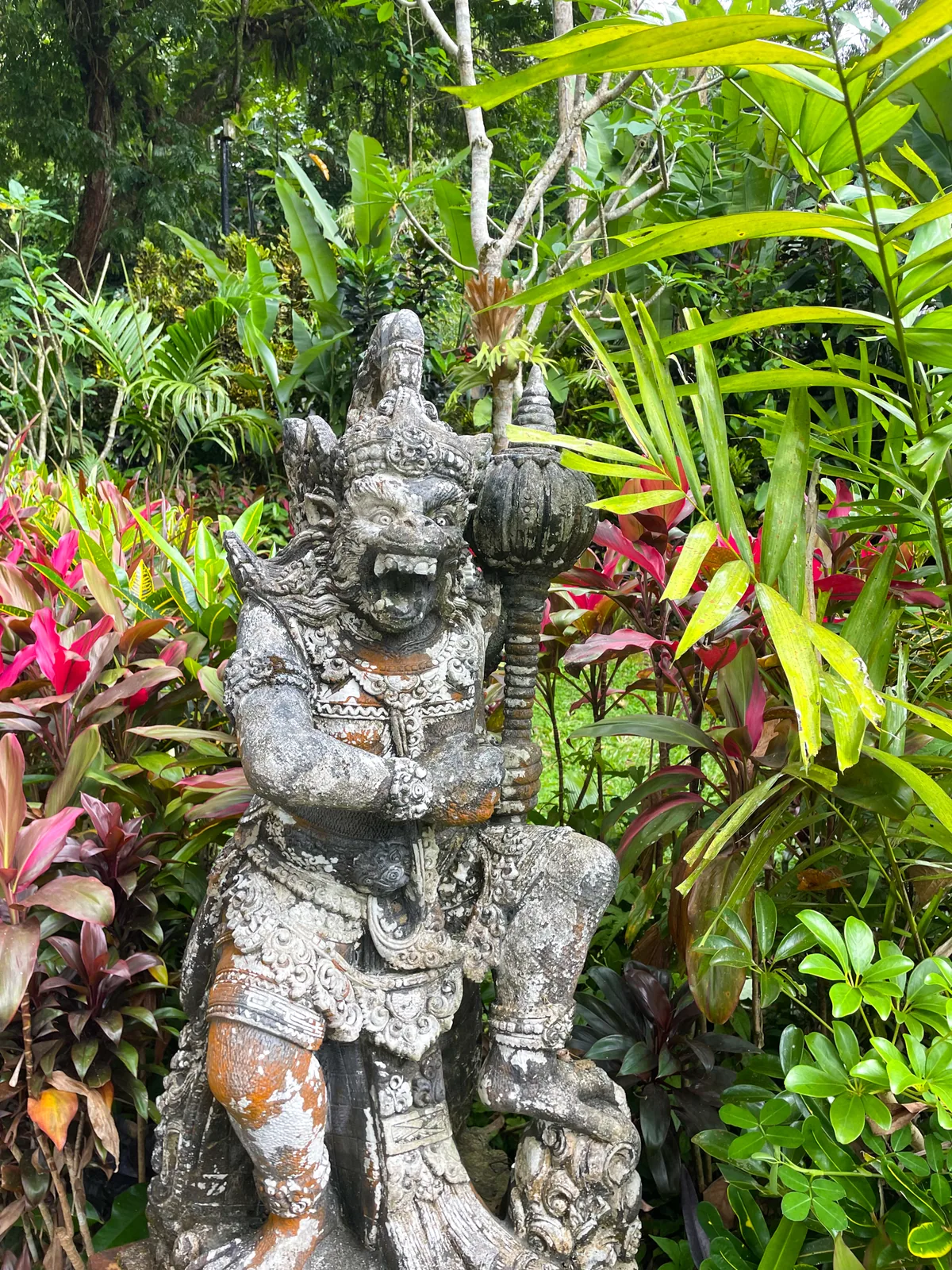 Stone guardian statue among red and green tropical plants