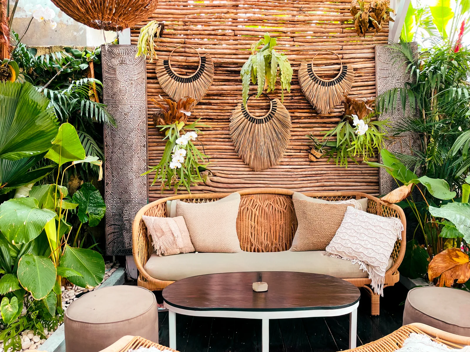 Boho lounge corner with a rattan sofa, macrame wall hangings and tropical plants
