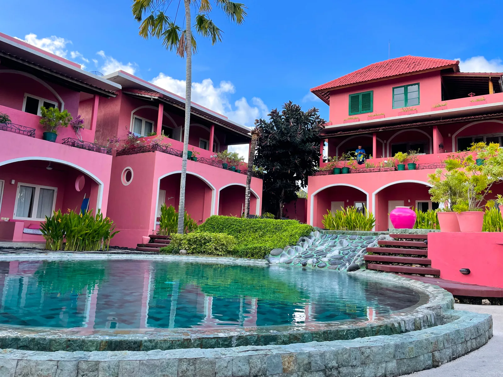 Pink Coco Uluwatu: pink buildings around the central pool, a palm tree and blue sky