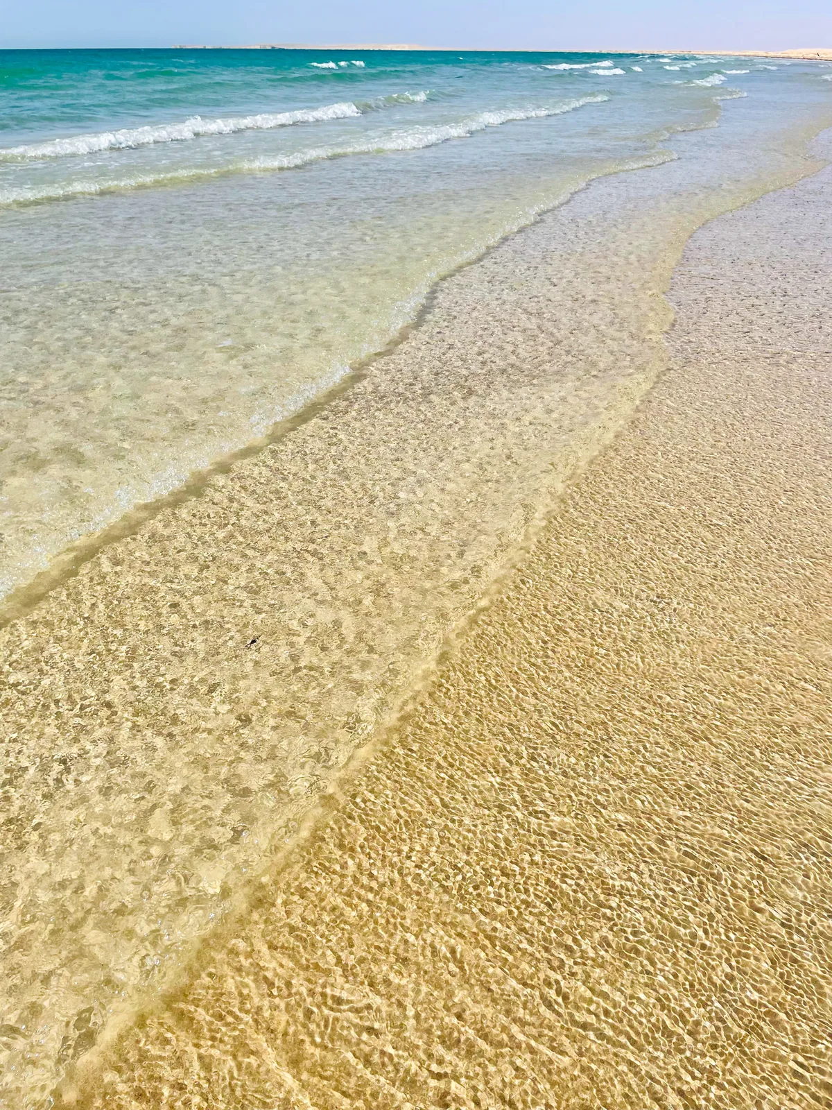 Glass-clear shallow water over rippled golden sand, with turquoise sea beyond