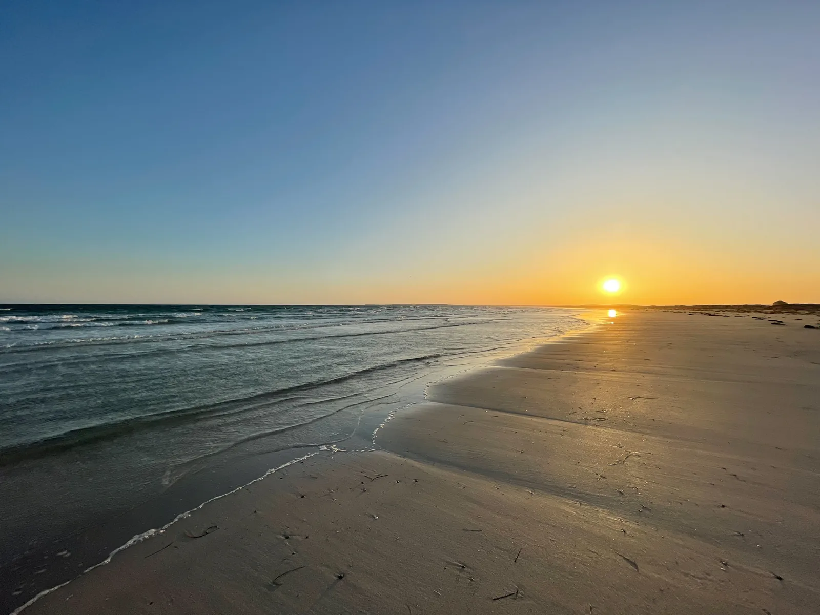 The sun setting low over a long empty beach, gentle surf on the left and wet sand glowing