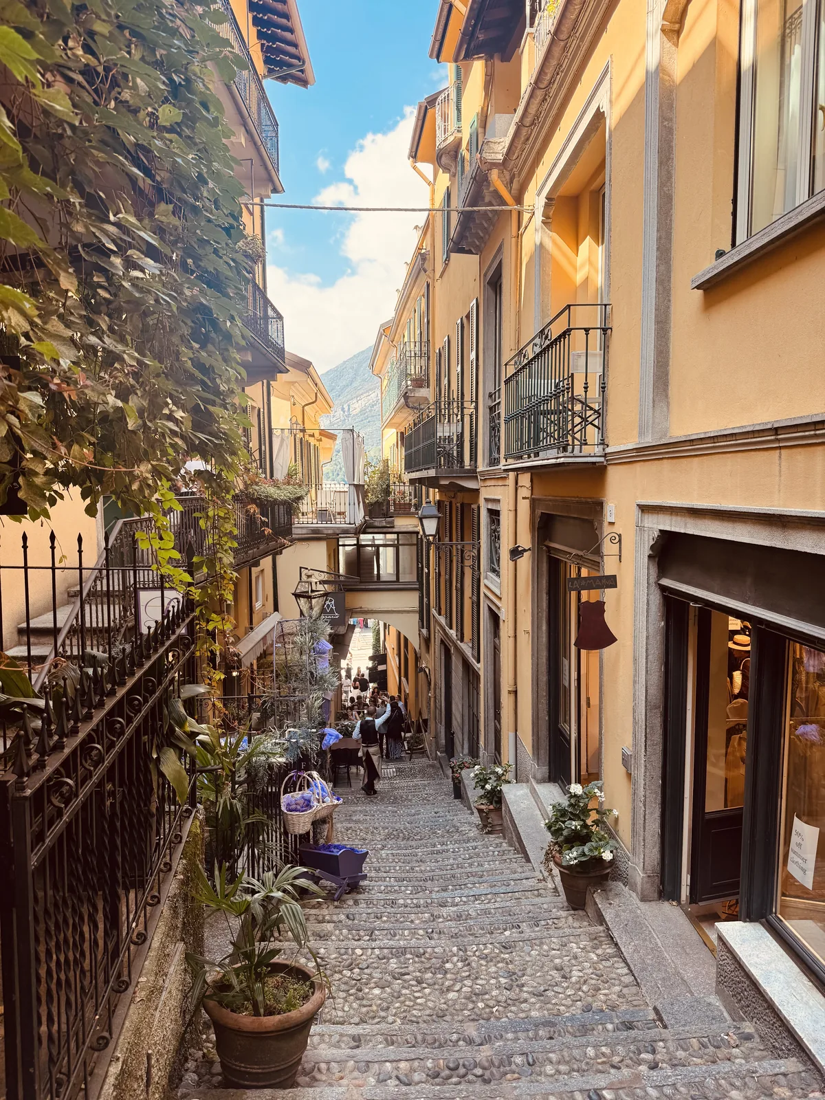 A second Bellagio alley with mustard-yellow buildings, potted plants and shoppers on the stairs