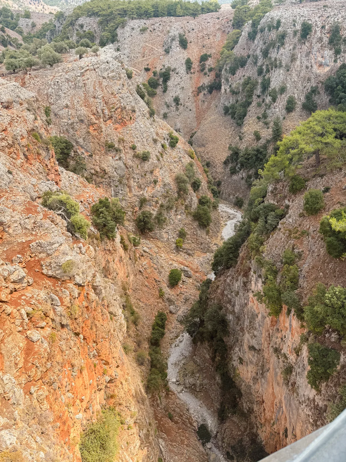 Looking straight down into the Aradena gorge from the bridge, red and grey walls above a dry riverbed