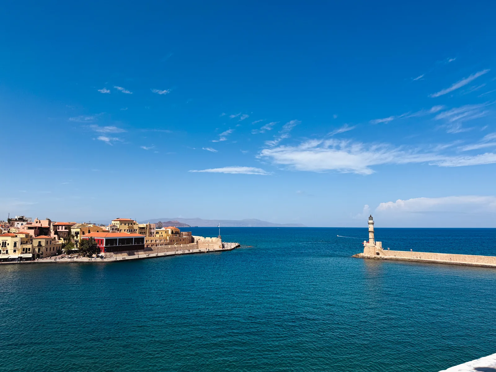 The Venetian harbour of Chania, the lighthouse on its breakwater and the harbour front across deep blue water