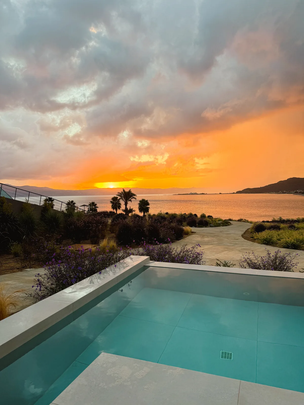 The same sunrise over a plunge pool, big orange and grey clouds above the bay