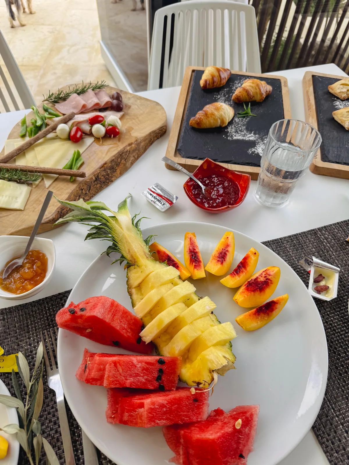 Breakfast plate of pineapple, watermelon and peach with croissants and jam