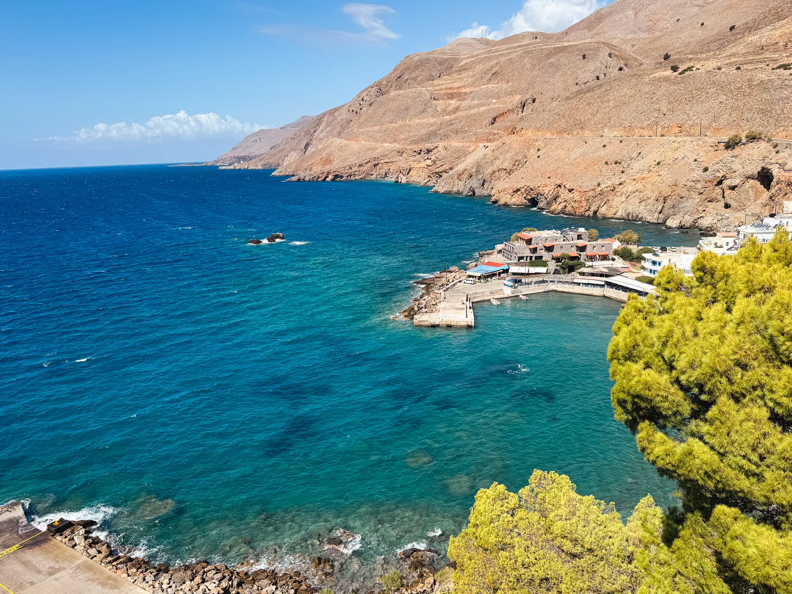 Chora Sfakion old harbour from above, tavernas and pine trees, the coast running west to the mountains