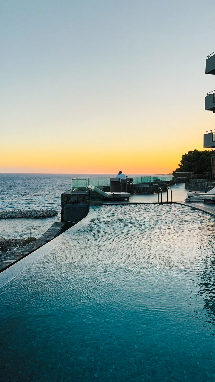 Sunset over the infinity pool and the breakwater, one person sitting at the pool edge