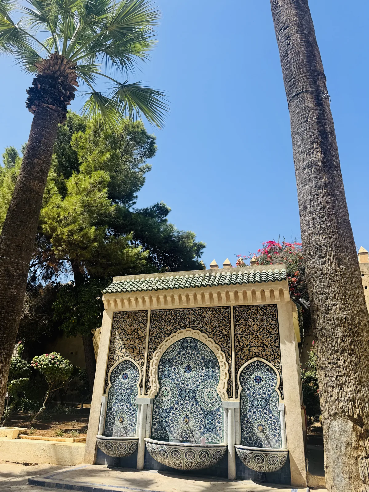 A tiled public wall-fountain in Fes framed by tall palms