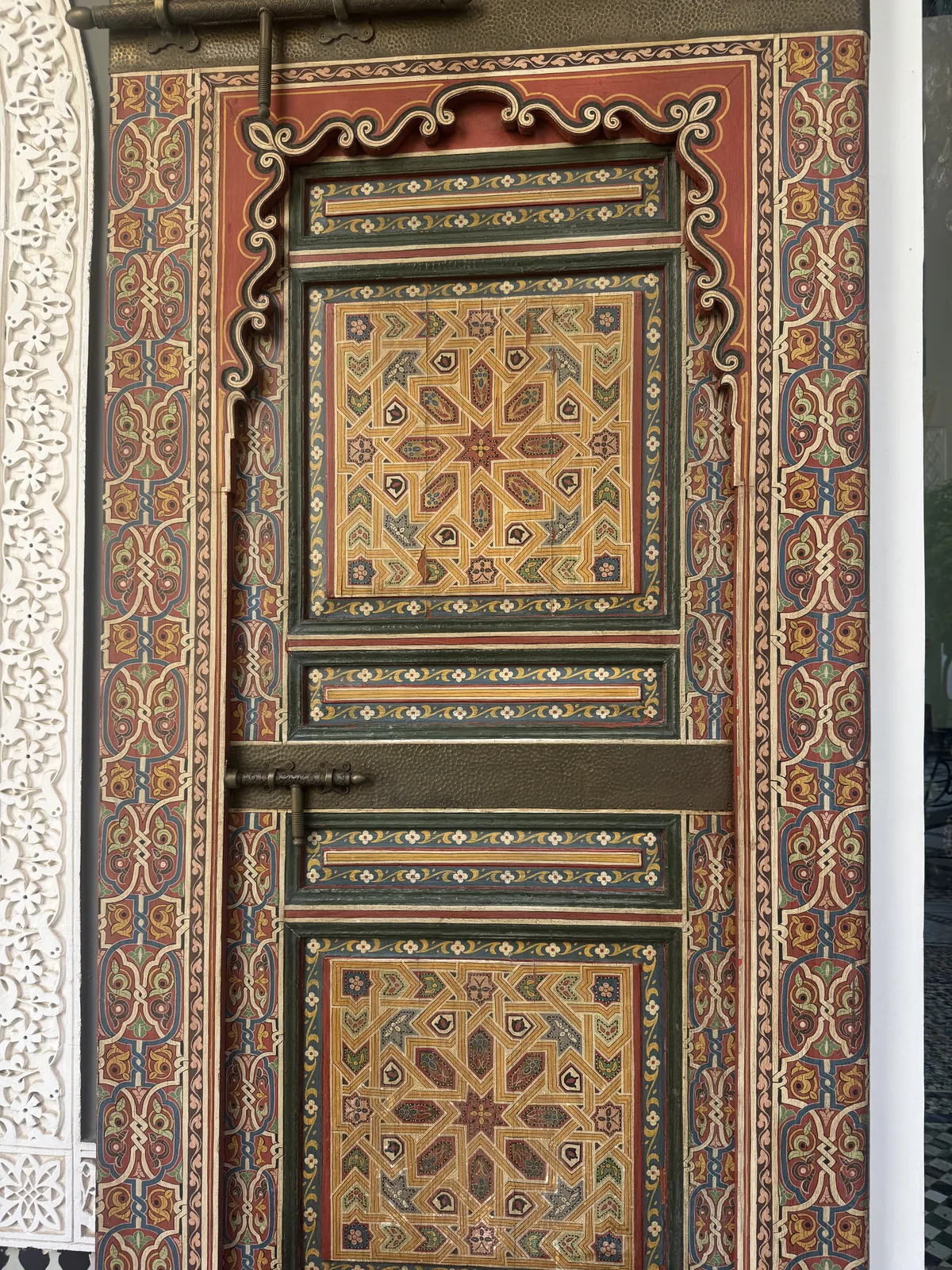 A close-up of an ornately painted Moroccan door in red, gold and green