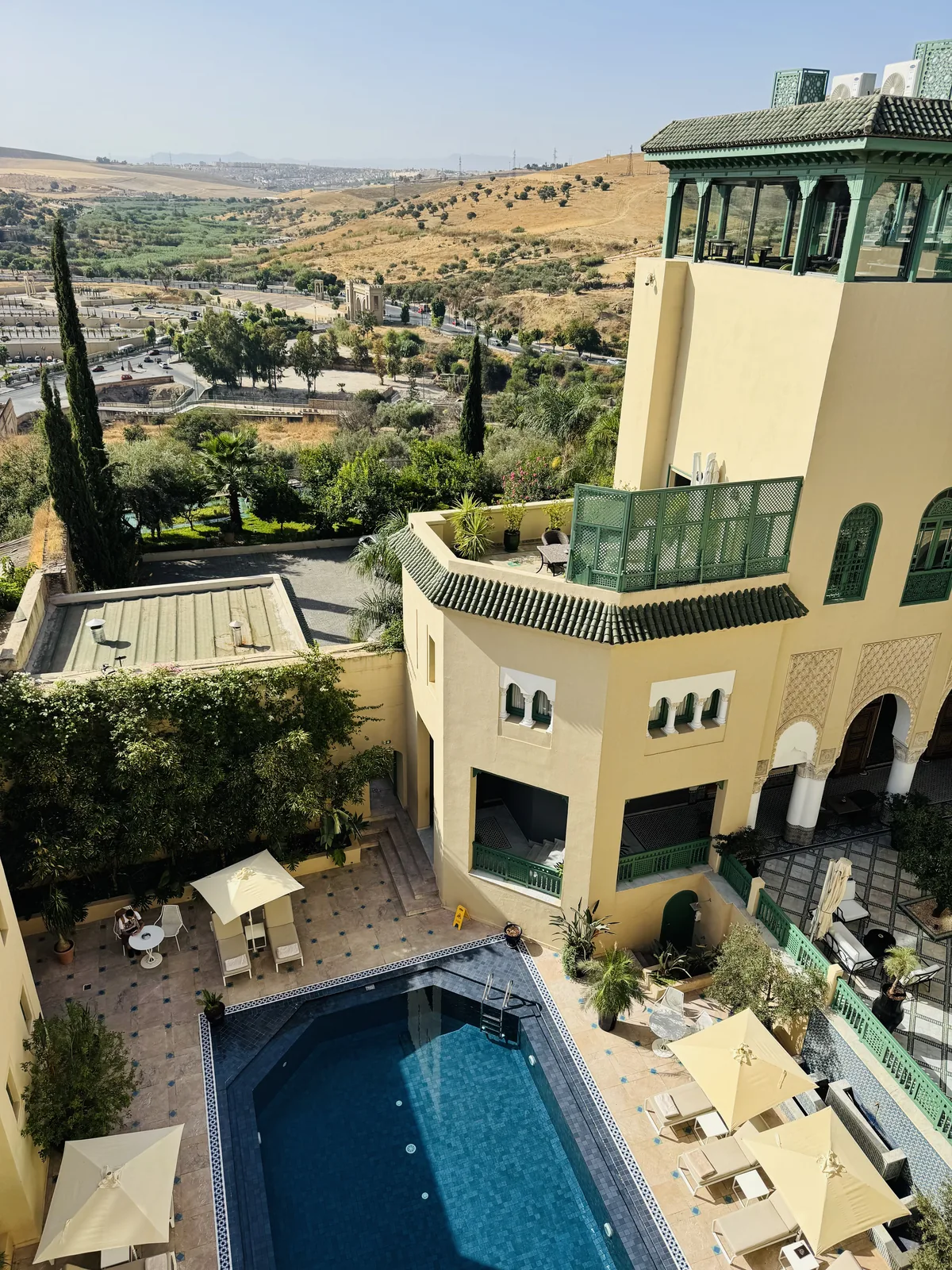 The Palais Faraj courtyard pool in daylight, green-tiled balconies rising around it with the Fes hills behind