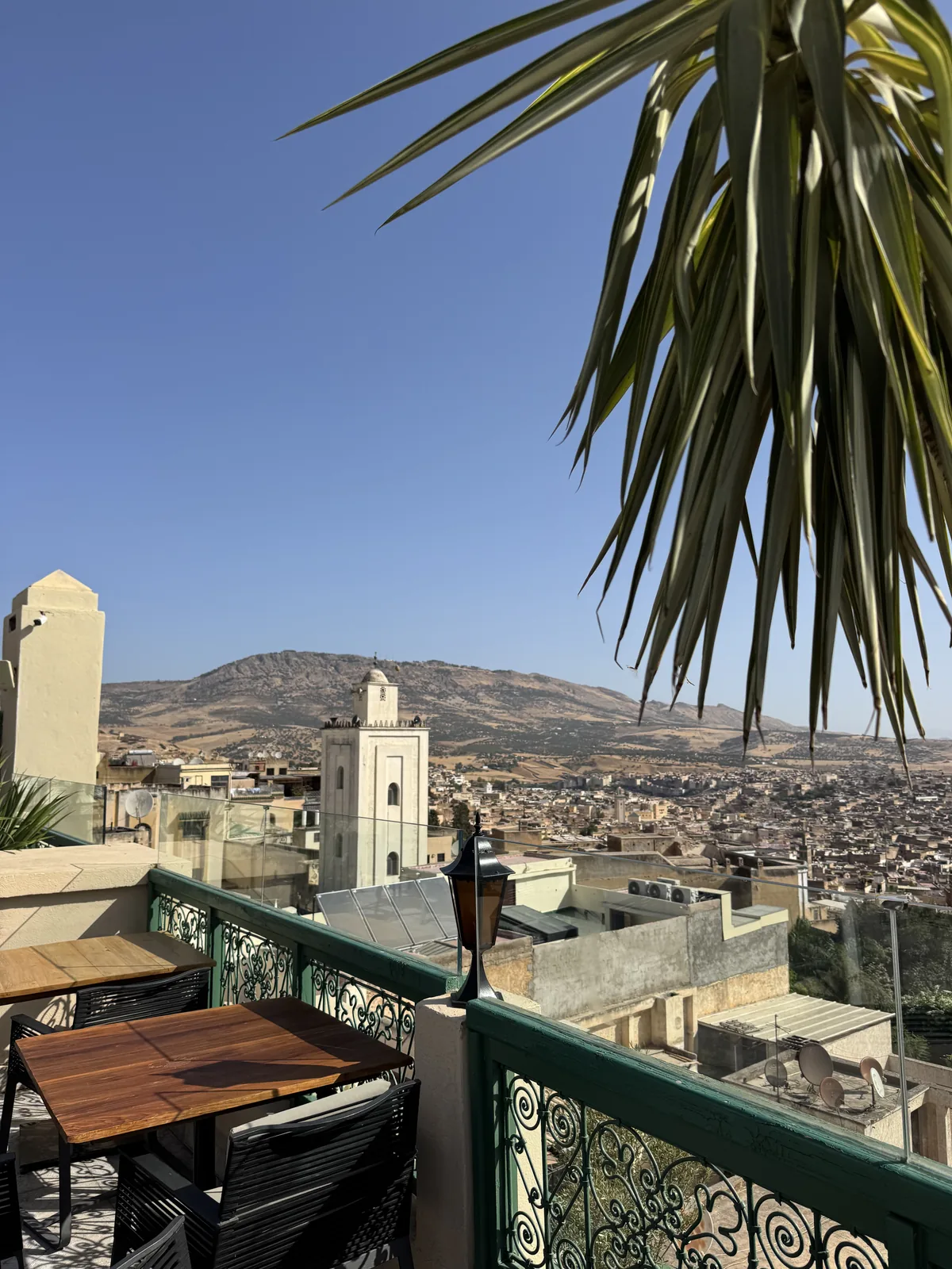 A rooftop terrace above the Fes medina at golden hour, a minaret and hills in the distance
