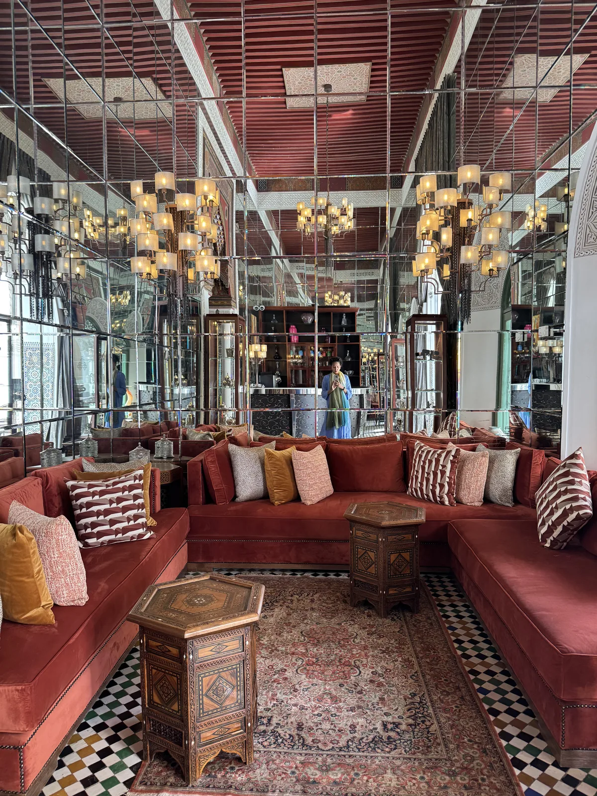 A mirrored salon with chandeliers and deep red velvet banquettes