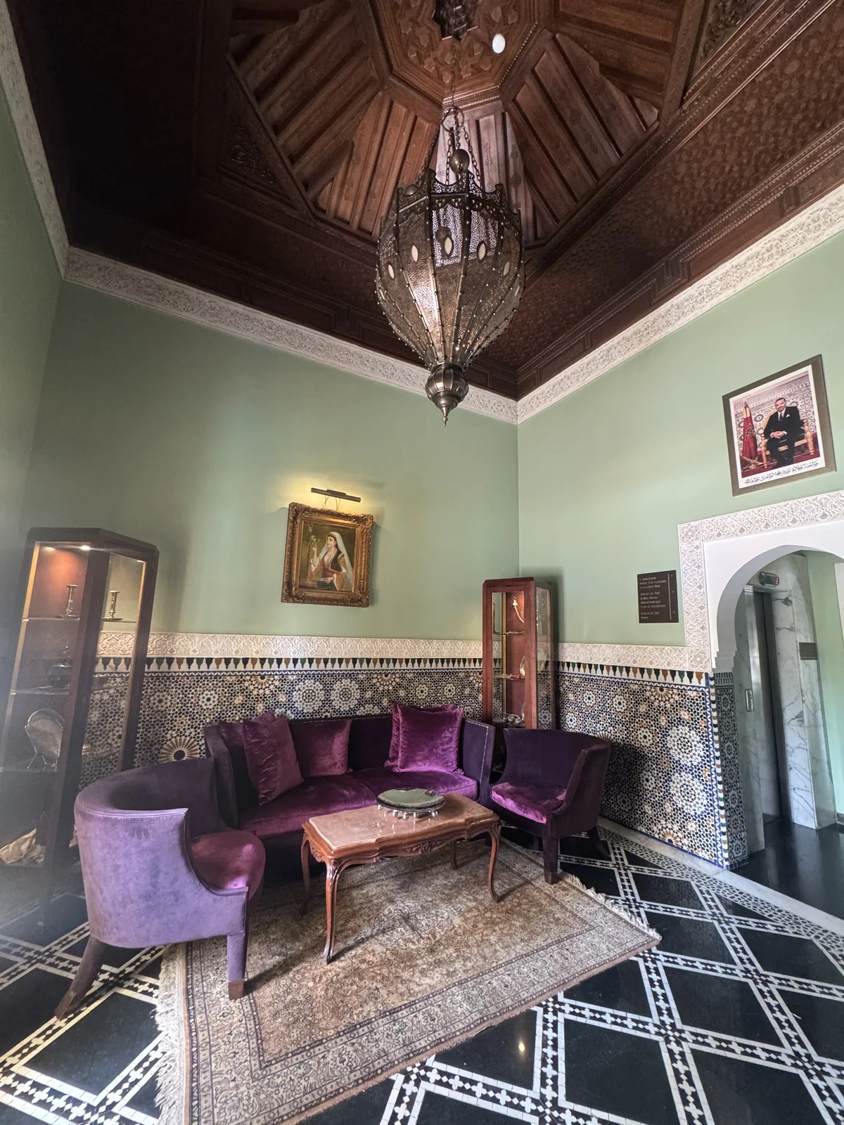A green-walled salon at Palais Faraj with zellige tiling, a carved cedar ceiling and purple velvet seating