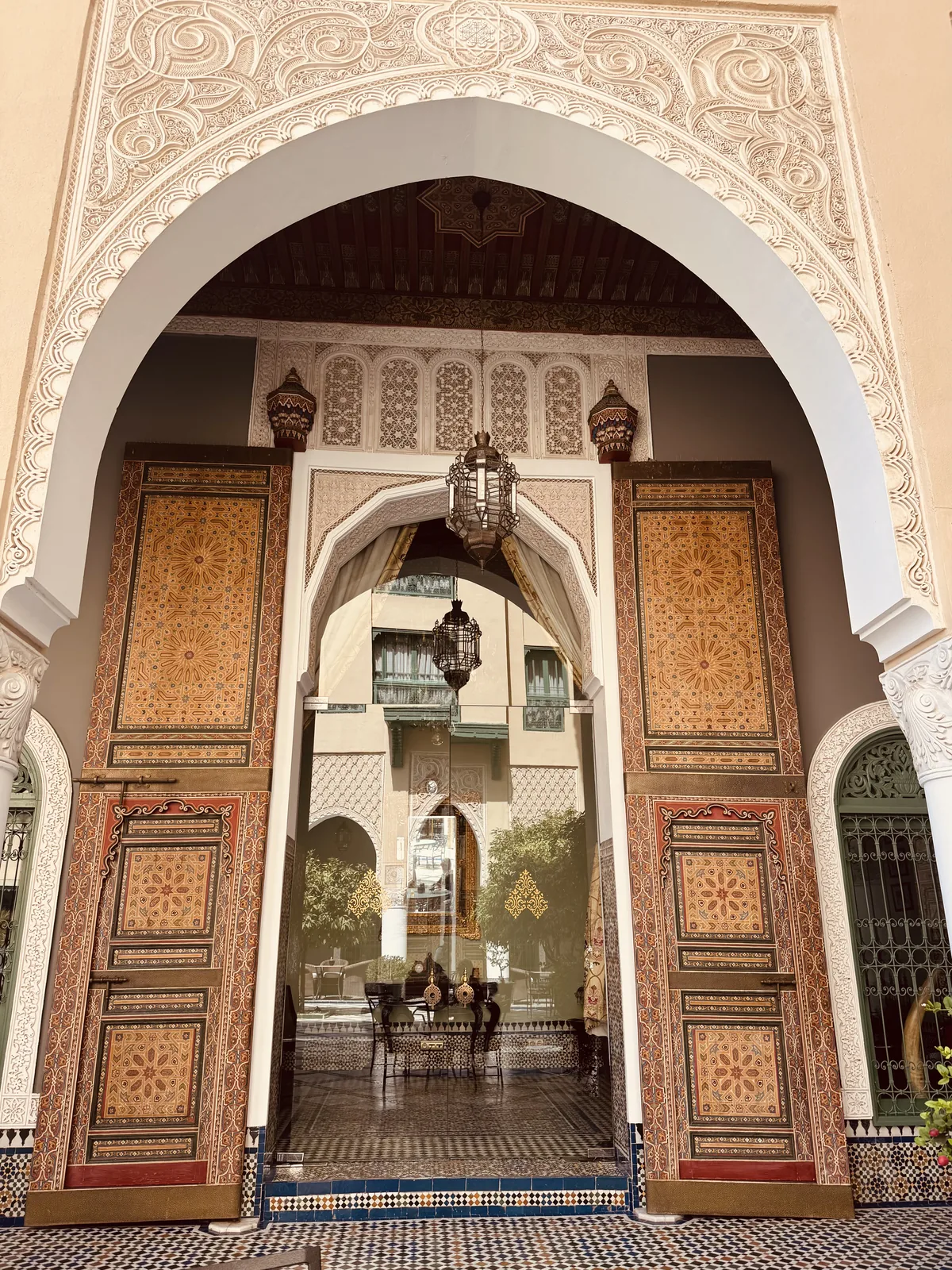 Ornate painted doors standing open onto a riad courtyard with a fountain