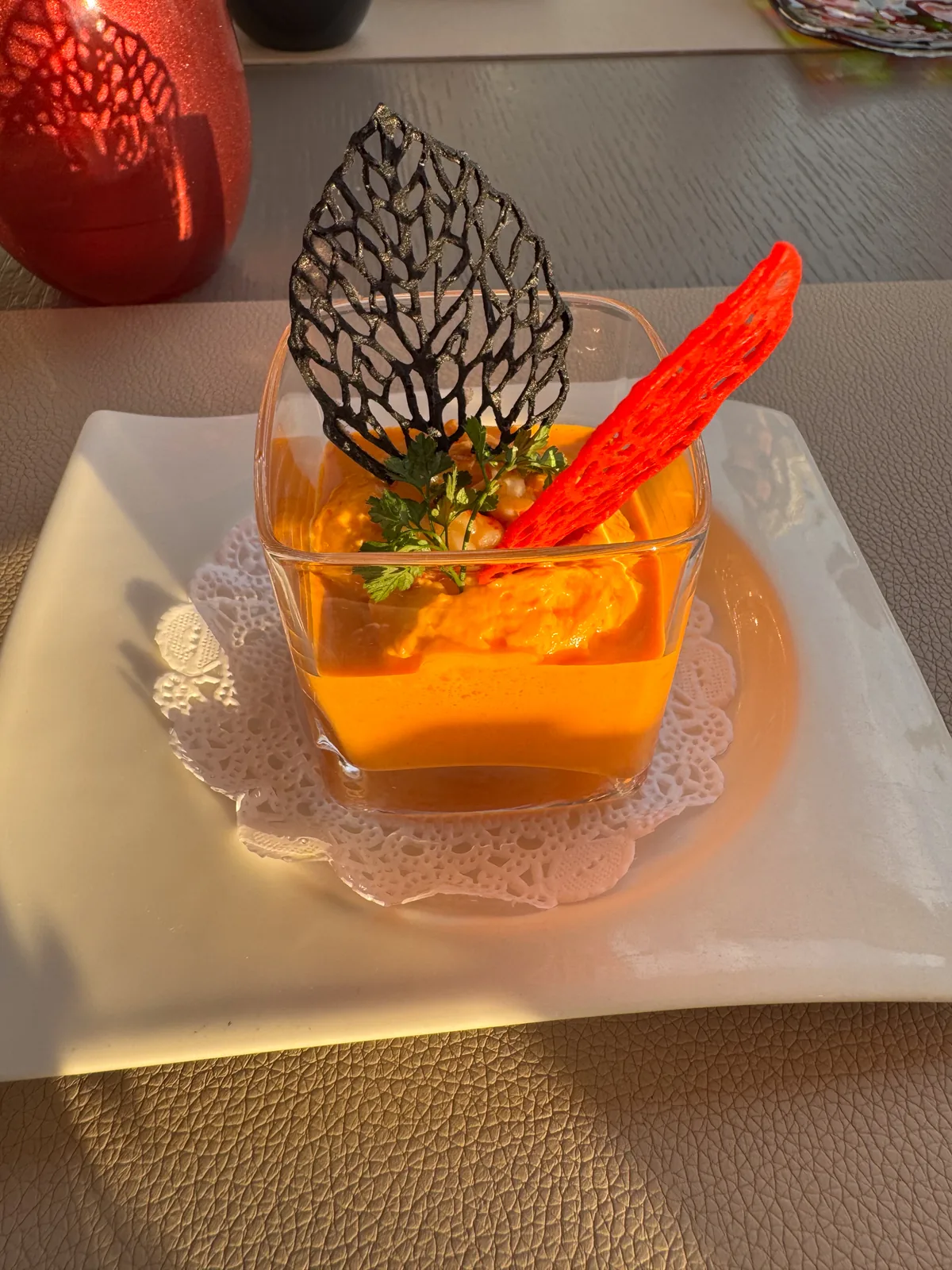 An orange verrine in a small square glass topped with a black lace tuile, in golden evening light