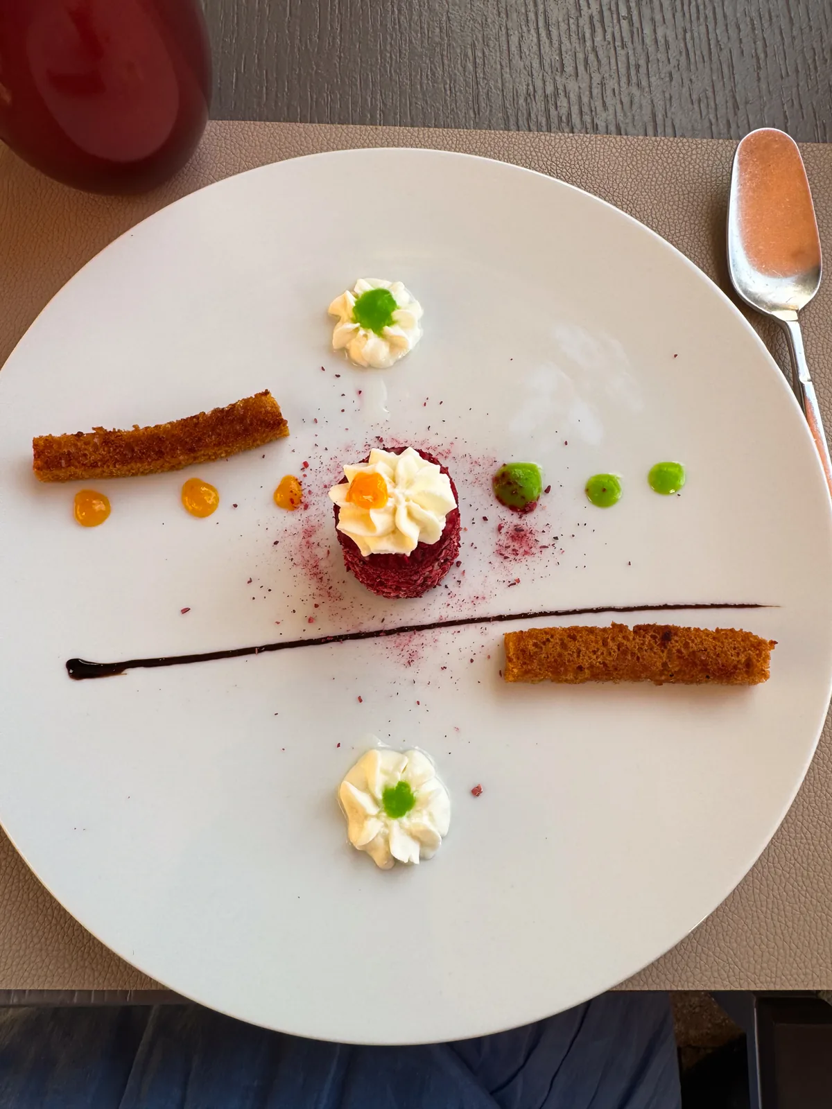 A small disc of beetroot tartare topped with cream, with toasted crouton fingers and dots of sauce on a white plate