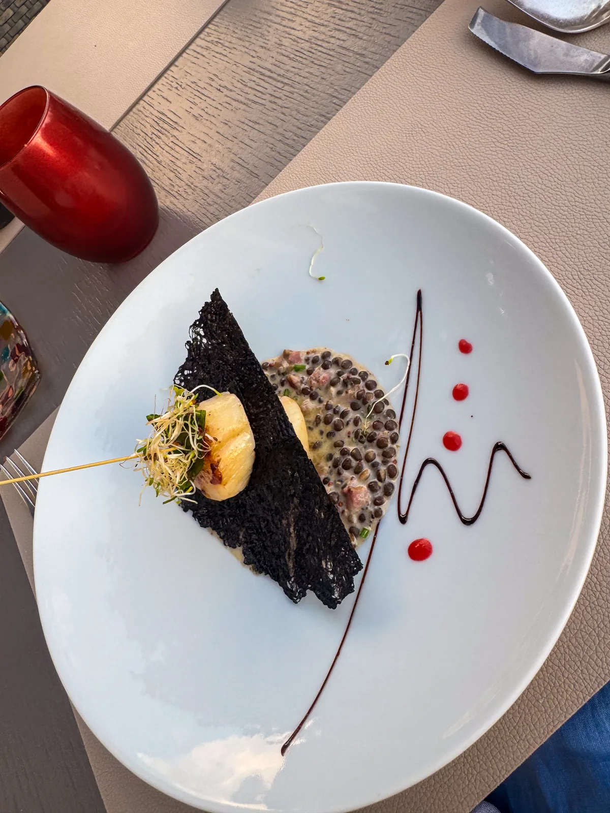 A seared scallop on lentils with a black squid-ink tuile and dots of red sauce