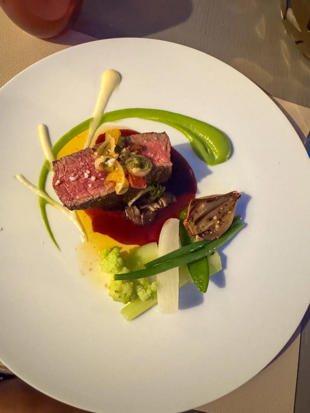 Slices of pink beef fillet with jus, a swoosh of pea purée and small spring vegetables