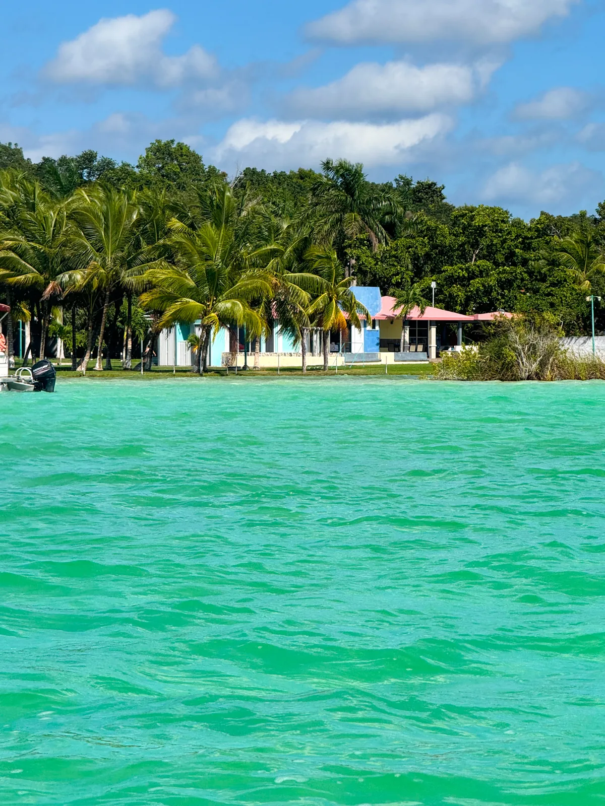 Bright turquoise lagoon water seen from the boat, a pink and blue house among the palms