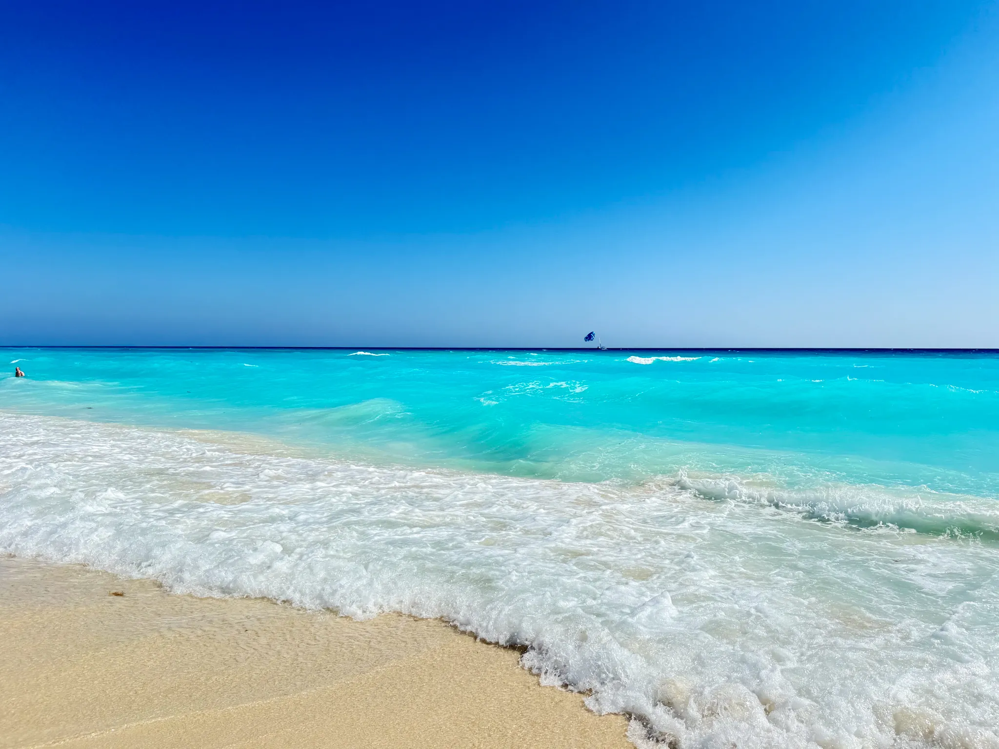 Bright turquoise surf breaking on white sand under a clear blue sky in Cancún