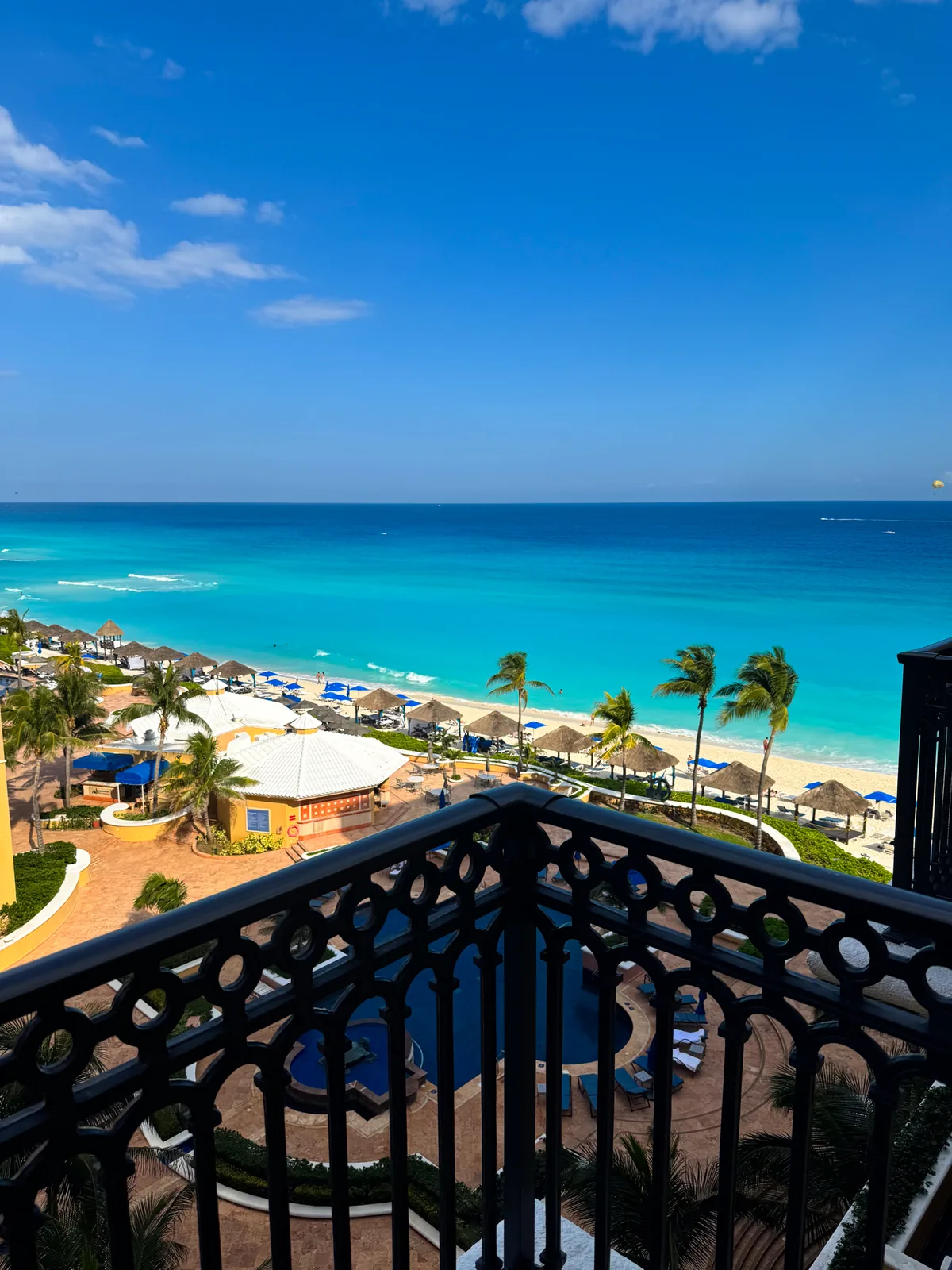 View from a wrought-iron balcony at the Kempinski Cancún over terracotta buildings, beach palapas and a turquoise sea