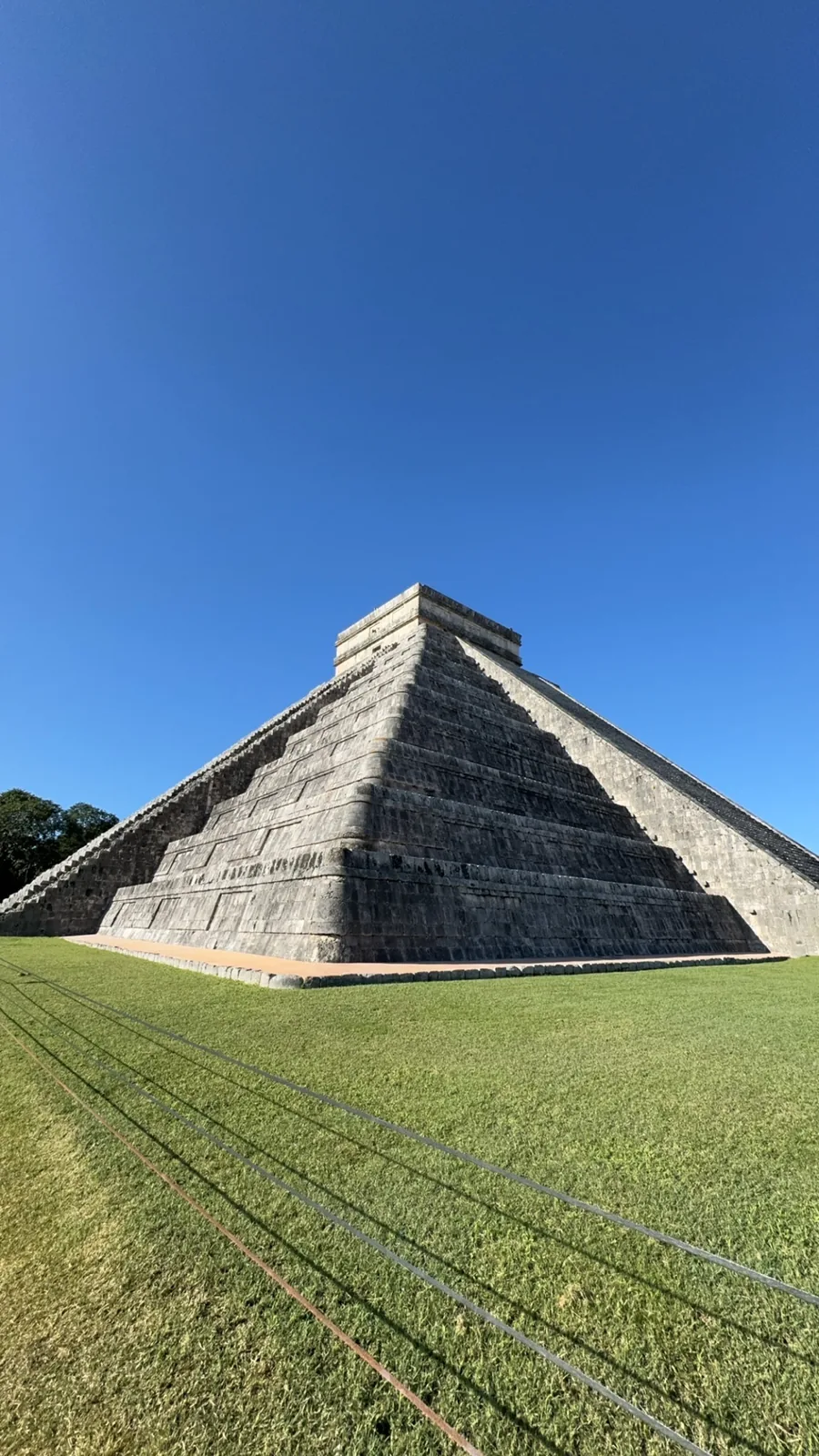 El Castillo at Chichén Itzá seen corner on, with an empty lawn and a deep blue sky