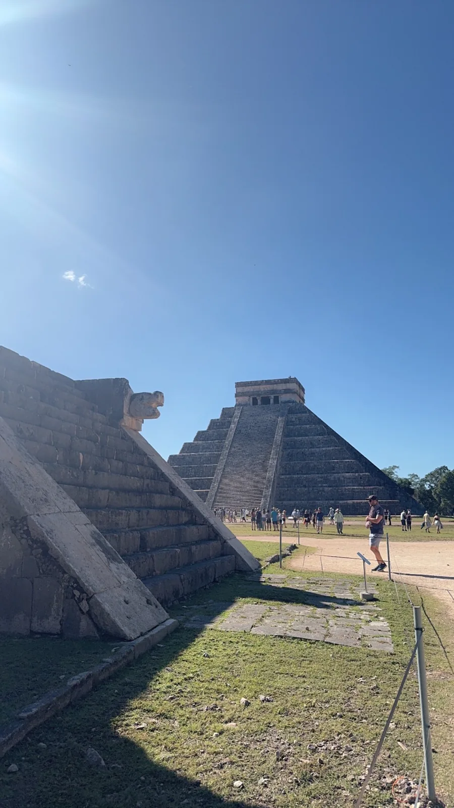 A carved serpent head on a platform in the foreground with El Castillo behind