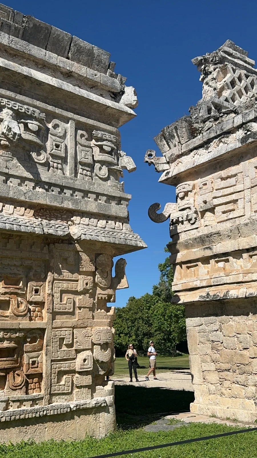 A narrow passage between two carved buildings of Las Monjas, two visitors walking through