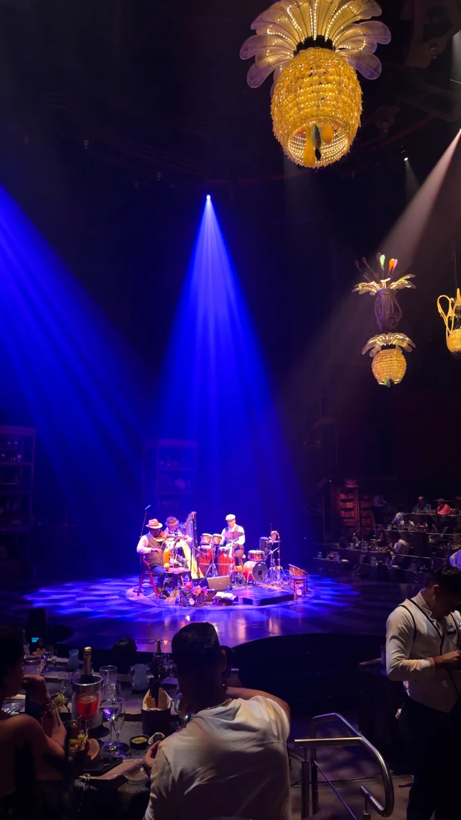 A live band on the round stage at JOYÀ under blue spotlights and pineapple chandeliers