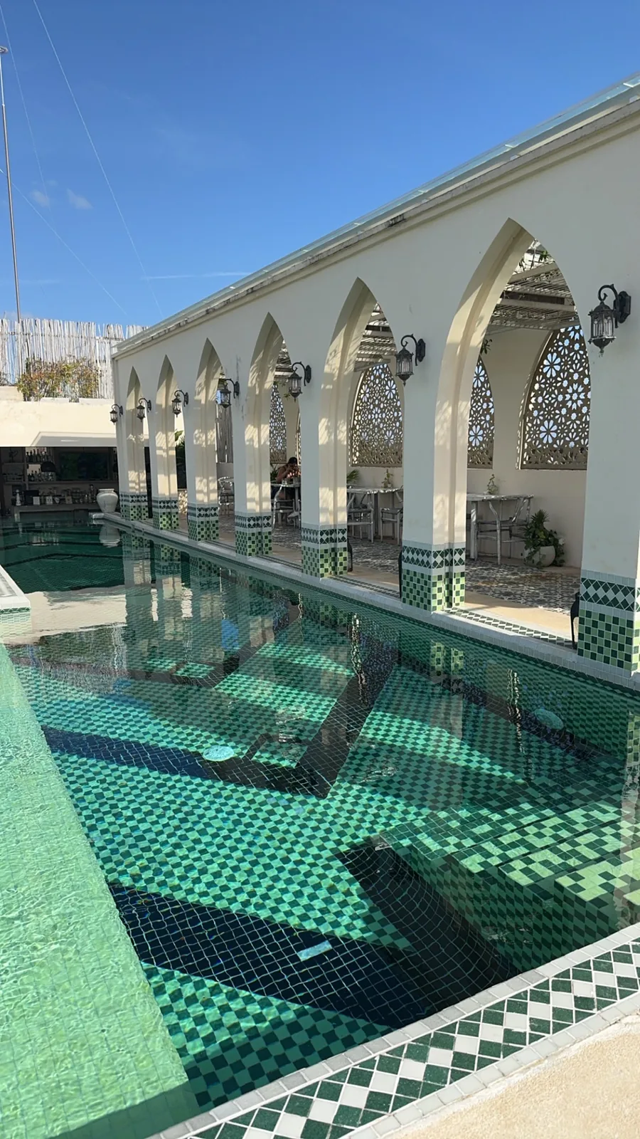 White Moroccan-style arches and lattice screens beside the green-tiled pool at Layla Tulum