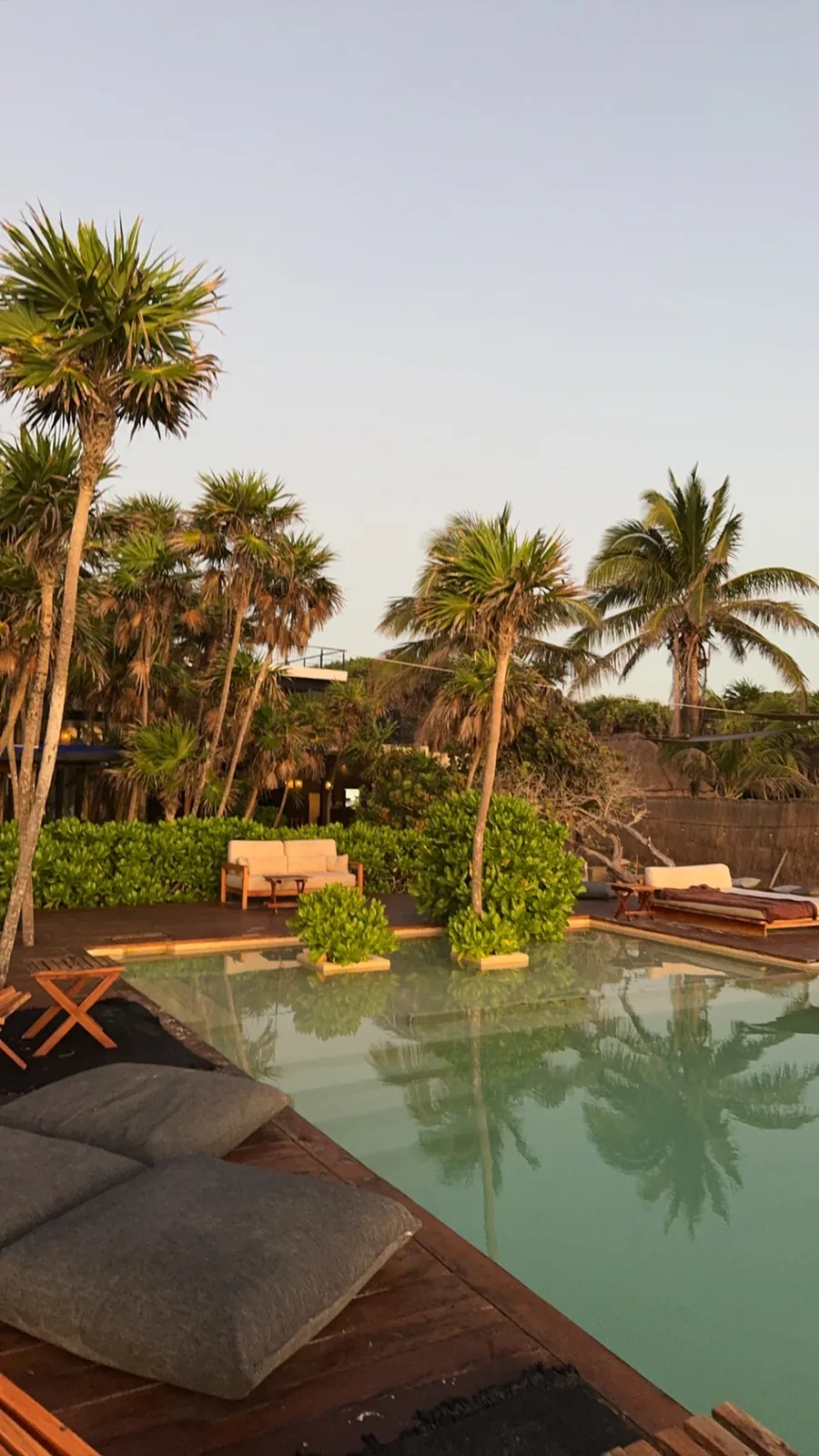 The Our Habitas pool deck at dawn with floor cushions, palms and a soft pastel sky