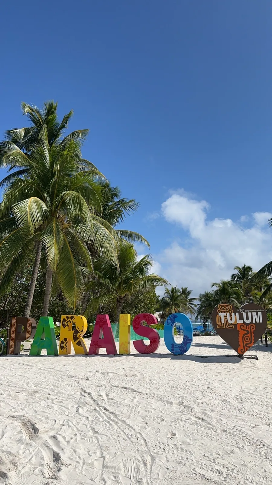 Colourful PARAISO letters and a TULUM heart on the white sand of Playa Paraíso, palms behind