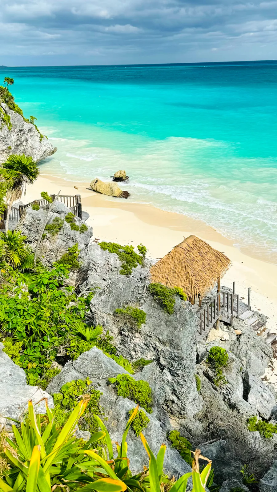Cliff-top view from the Tulum ruins down to a small beach, a thatched hut and the turquoise sea