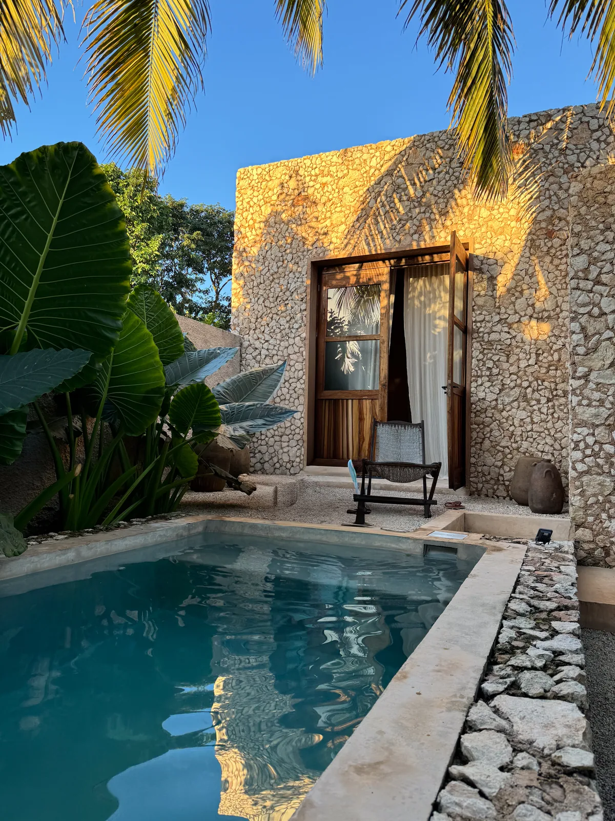 The same pool and wooden door in golden early-morning light with palm shadows