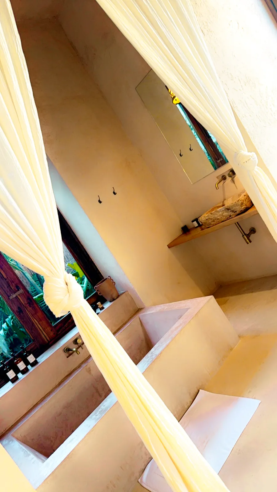 A warm tadelakt bathroom with a sunken tub and a gauzy curtain