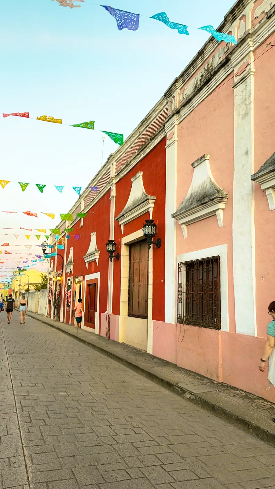 Pink and red colonial facades on Calzada de los Frailes in Valladolid, papel picado strung overhead