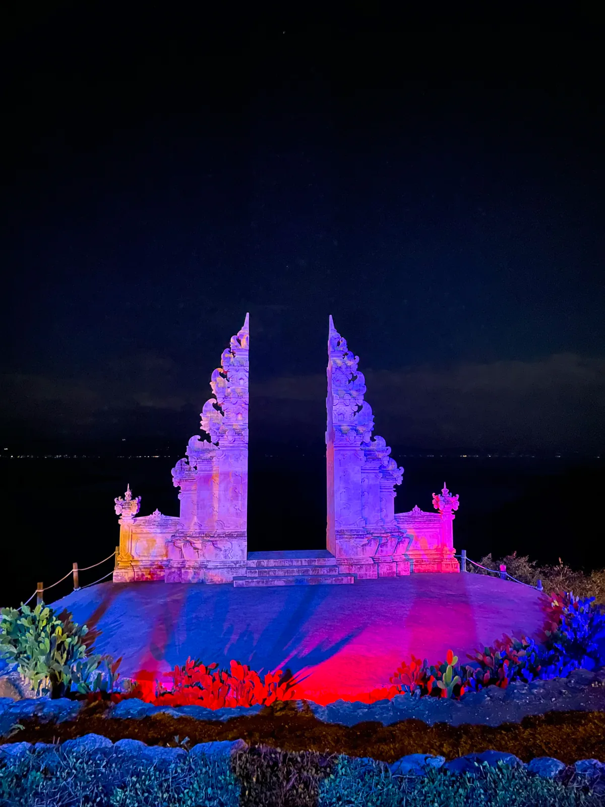 A Balinese split gate lit pink and purple at night.