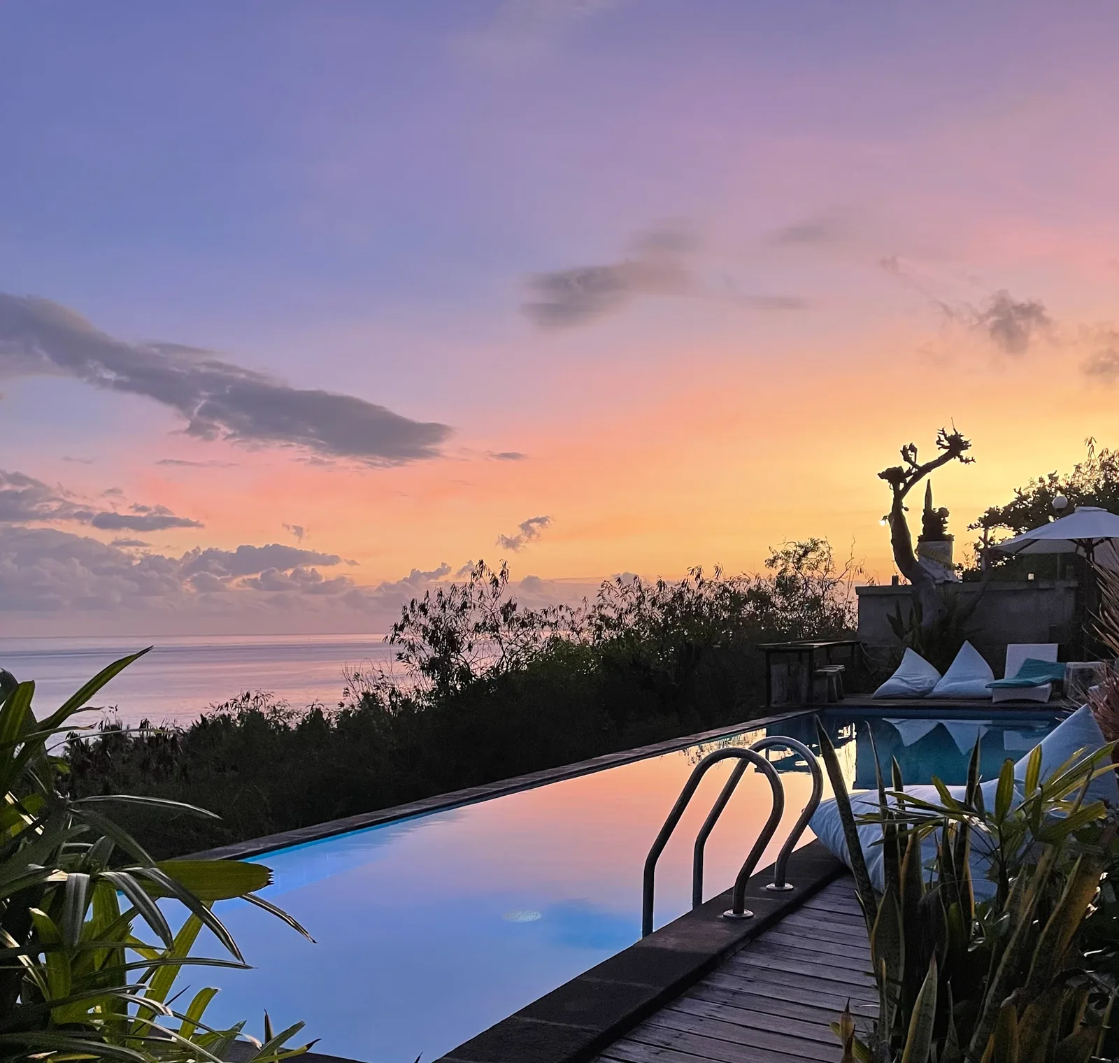 The infinity pool at dawn under a pink and orange sky, a statue in silhouette.