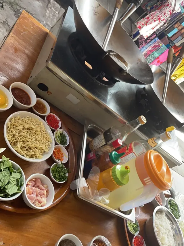 A cooking-class station laid out with bowls of noodles, chopped vegetables and sauces beside a wok